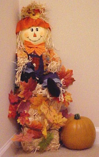 scarecrow sits on straw bale with leaves and pumpkin